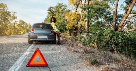 woman with broken car and triangle waiting for a jump start